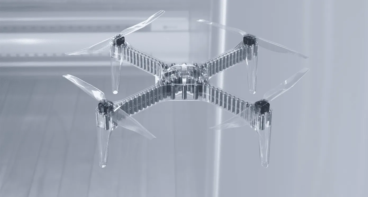 A quadcopter drone with a transparent frame and propellers, hovering in a light room